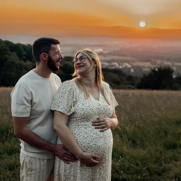 Babybauchshooting: werdende Eltern im Abendlicht auf einer Wiese mit Blick über das Tal