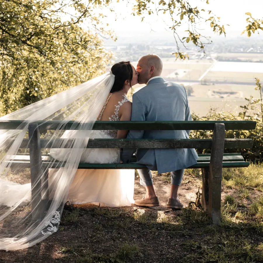 Hochzeitsfotografie in Freiburg: Brautpaar küsst sich auf einer Holzbank mit Blick über das Tal